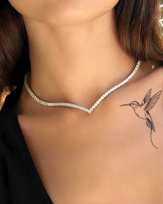 Primo piano di donna che indossa la collana tennis a V ÉCLAT con zirconi e tatuaggio colibrì.