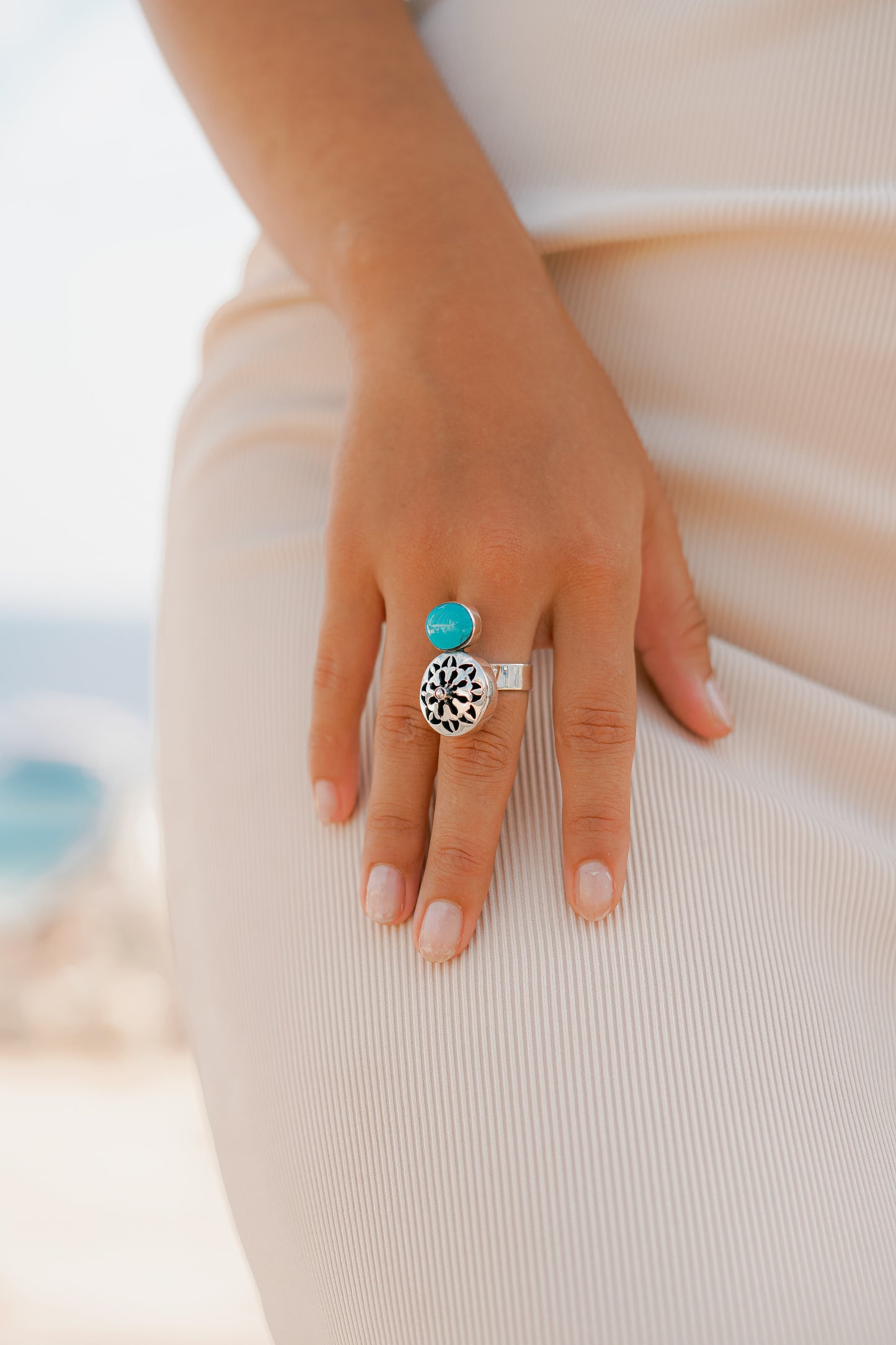 "Dettaglio mano con Anello Segreto di Siwa in Argento 925 e Turchese. Design con rosone traforato e fascia regolabile, indossato su un outfit dai toni neutri. Collezione Siwa Éclat Gioielli."