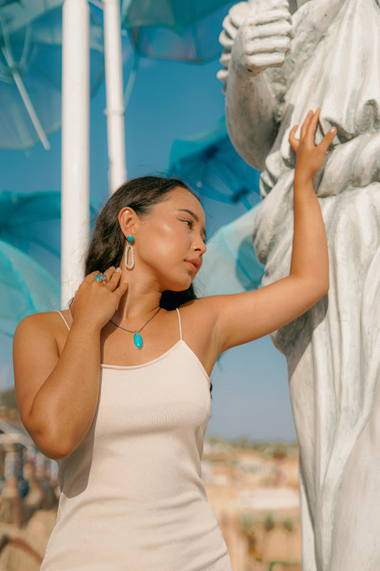 "Modella indossa gioielli Éclat della Collezione Siwa in Argento 925 e Turchese. Un look estivo raffinato con collana pendente e anello coordinato, perfetto per uno stile solare."