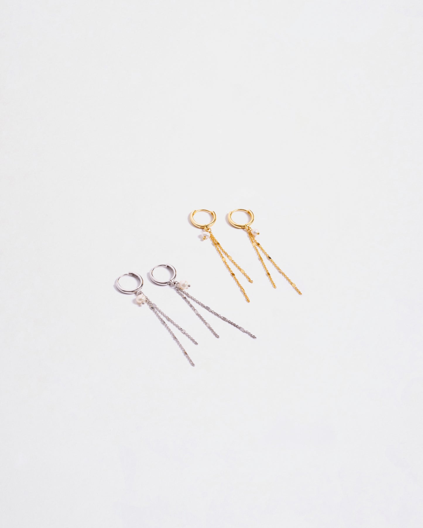 Due paia di orecchini pendenti in argento sterling 925, uno color argento e uno placcato oro, entrambi con catenine e perle, disposti su sfondo bianco."