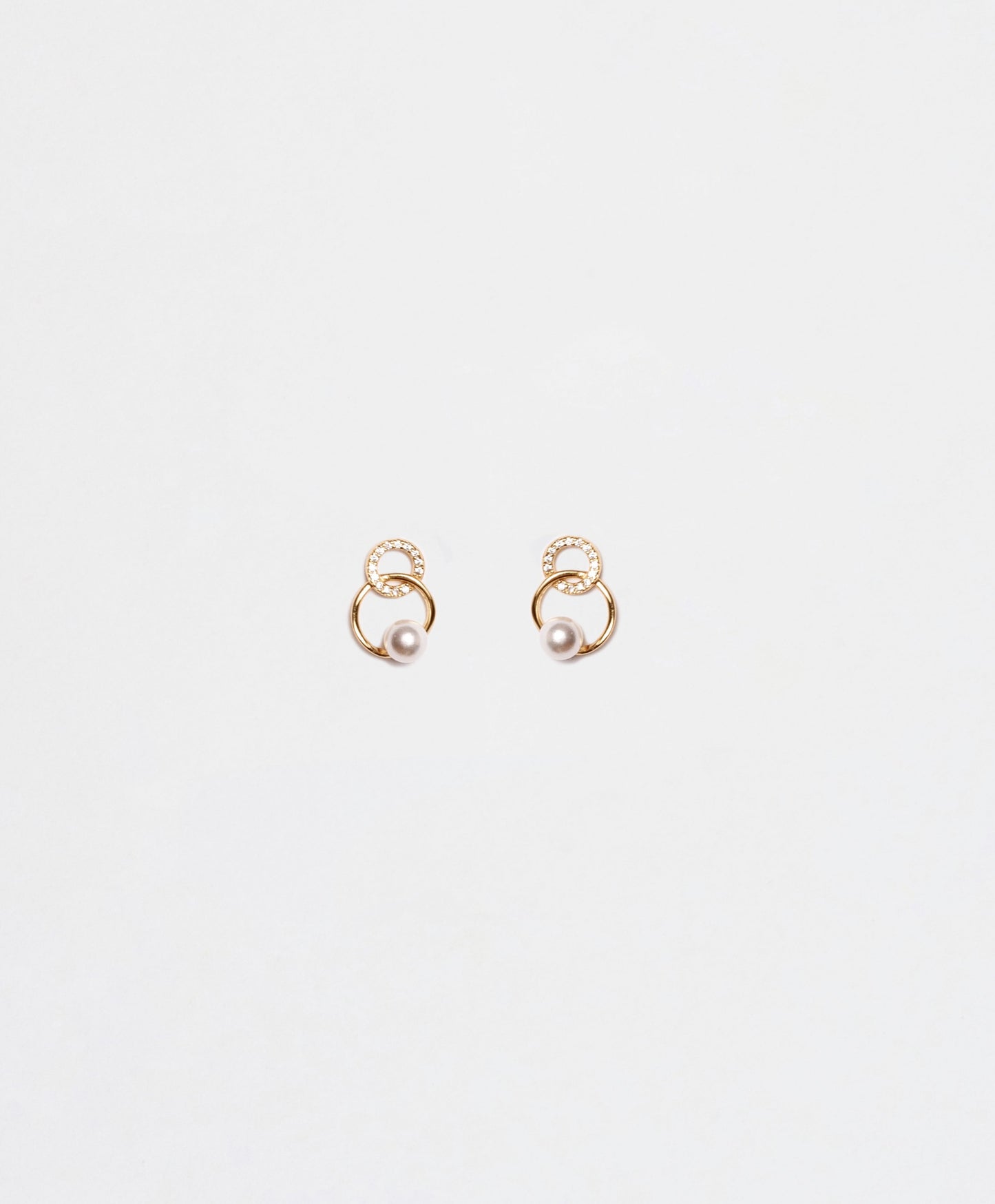 Un paio di orecchini a perno in argento 925 placcato oro, con doppio cerchio intrecciato e una perla pendente. Un cerchio è liscio, l'altro è decorato con zirconi. Su sfondo bianco."