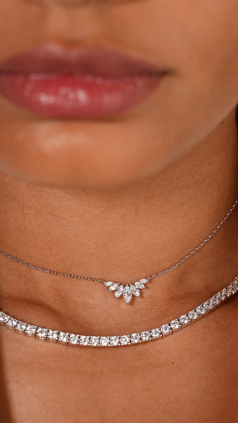 Gros plan d'une femme portant deux colliers, un collier tennis 3mm en argent 925 avec zircons scintillants et un collier fin avec pendentif feuille, sur une veste blanche. Bijoux Eclat.