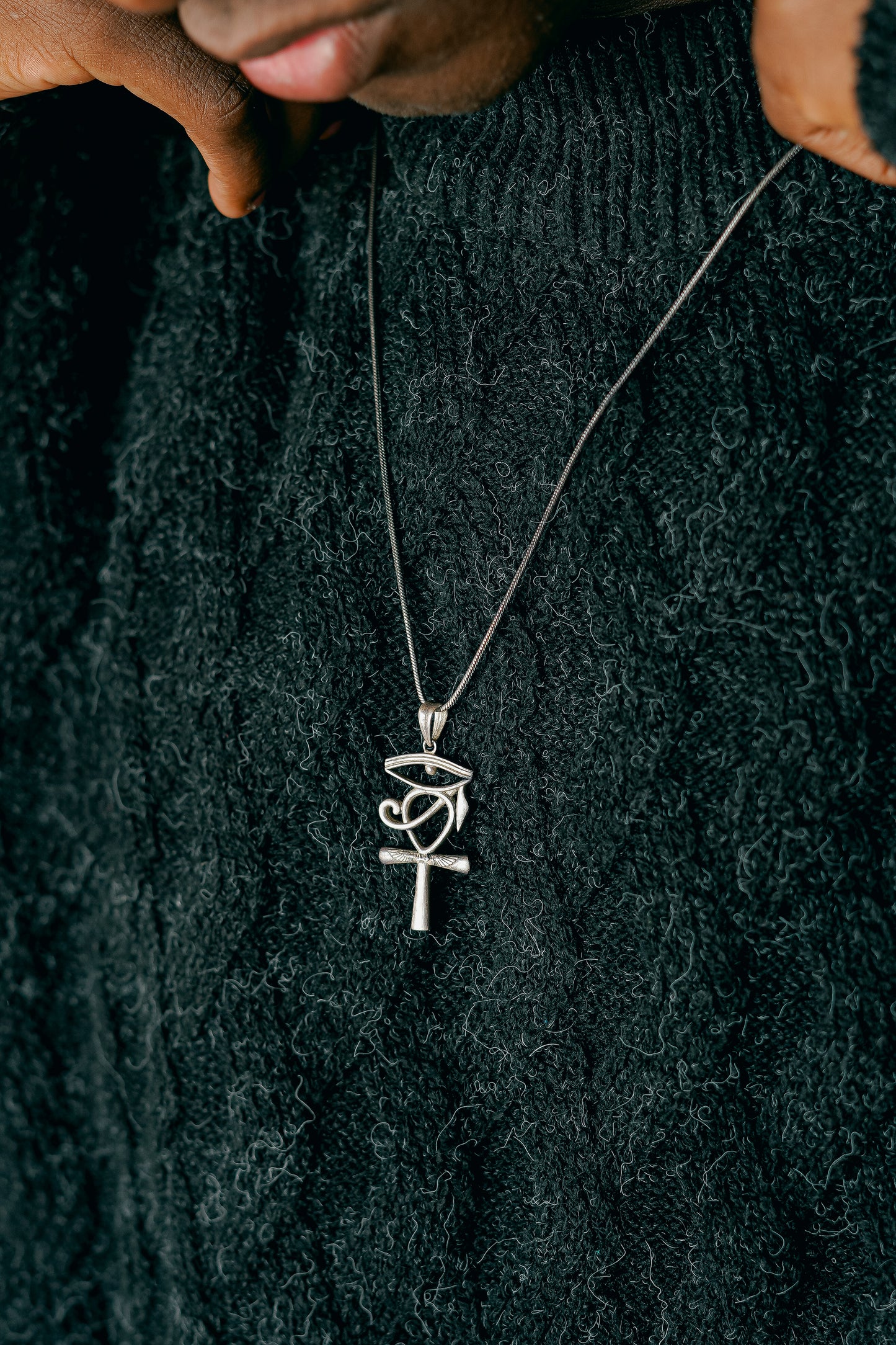 Sterling 925 Silver Egyptian Ankh and Eye of Horus pendant, worn on a chain. Close-up of the pendant against a dark, textured knit sweater.