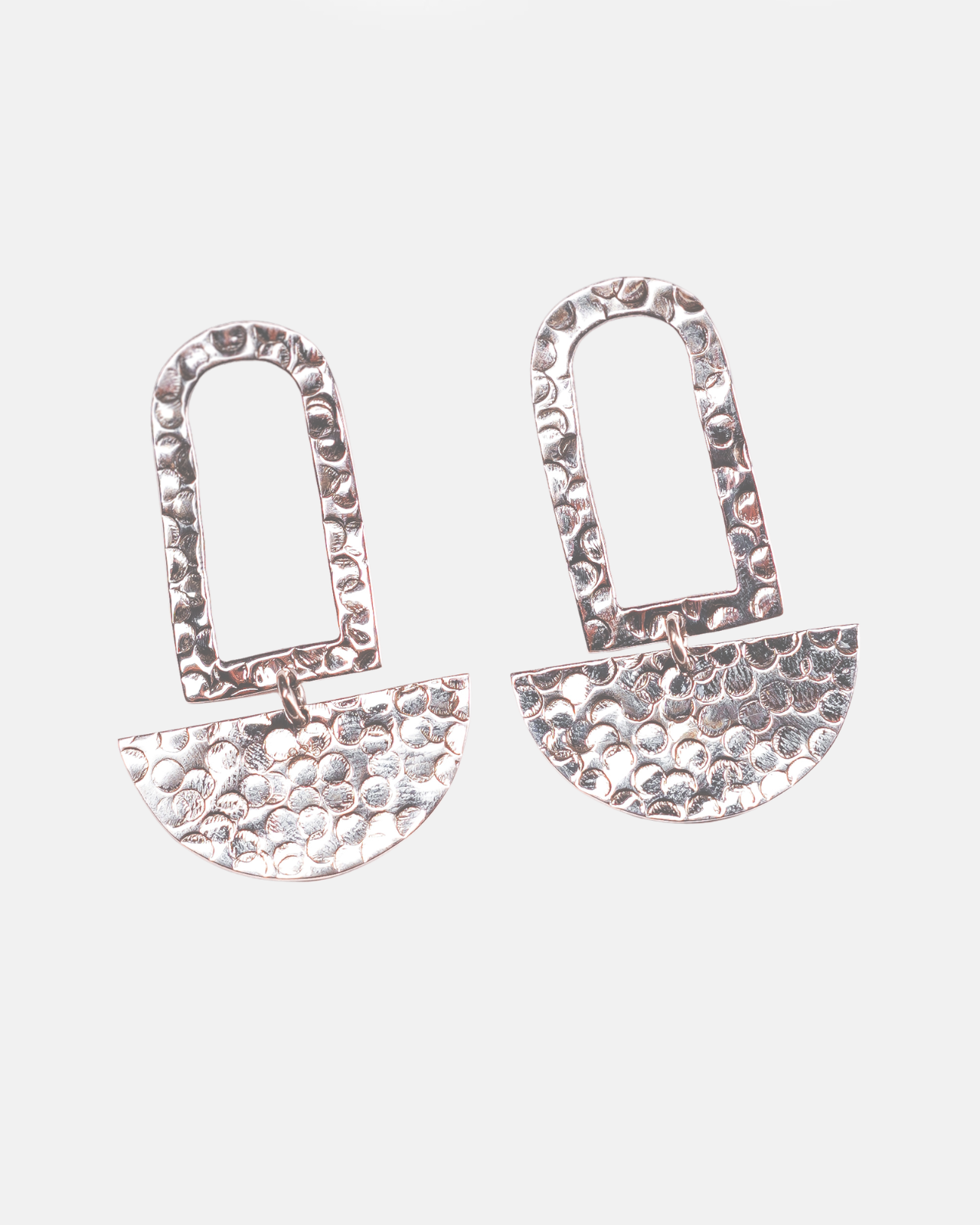 Coppia di orecchini pendenti in Argento 925 martellato a mano Éclat Gioielli Collezione Siwa. Il design presenta una forma a arco geometrico superiore e un elemento a semicerchio martellato inferiore che ricorda una luna calante, su uno sfondo grigio chiaro pulito. Gioielli artigianali in argento martellato."