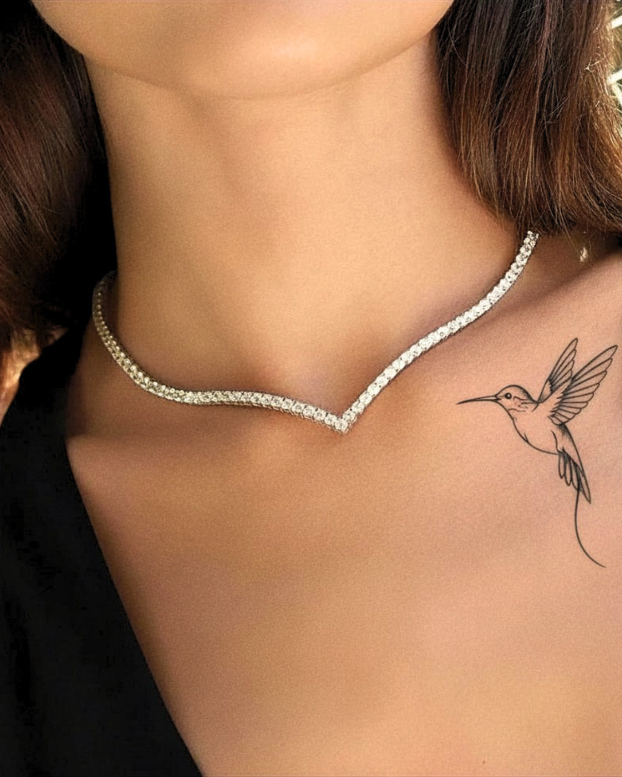 Primo piano di donna che indossa la collana tennis a V ÉCLAT con zirconi e tatuaggio colibrì.