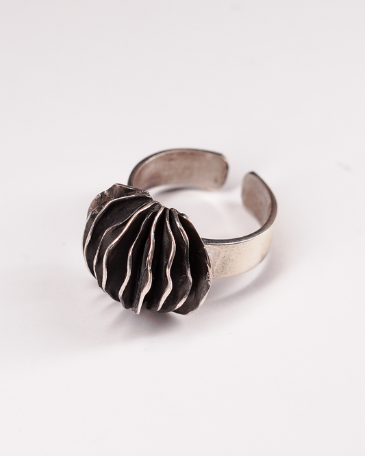Anello regolabile in Argento 925 Éclat Gioielli Collezione Siwa, modello Guscio di Shali. Il design scultoreo presenta lamelle sottili e ondulate sovrapposte con finitura brunita negli incavi e profili lucidi, evocando una forma organica e stratificata. Gioiello artigianale su sfondo bianco."