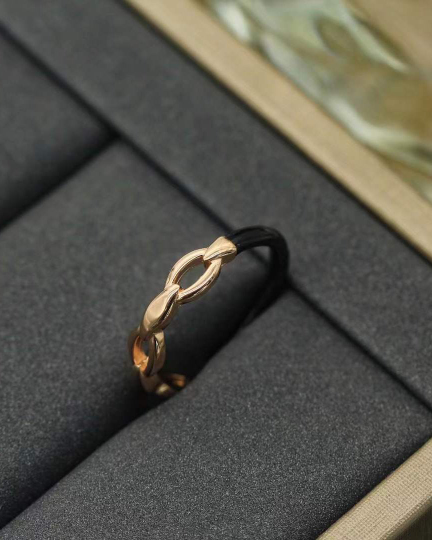 "Anello a fascia aperta in Argento 925 con design a maglie intrecciate. Colore argento lucido. Presentato su una superficie scura con una scatola per gioielli chiara sullo sfondo e una bottiglia di profumo."