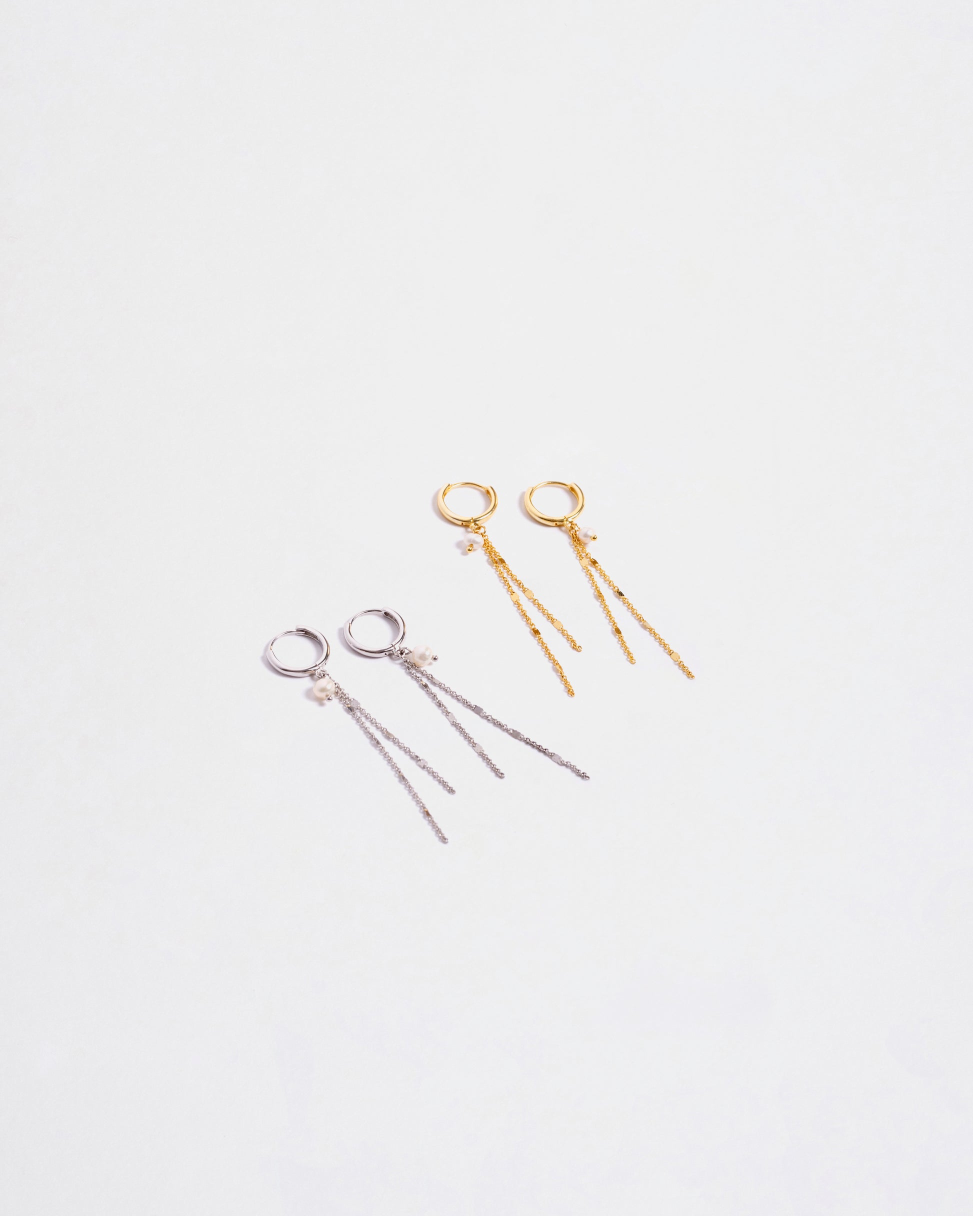 Due paia di orecchini pendenti in argento sterling 925, uno color argento e uno placcato oro, entrambi con catenine e perle, disposti su sfondo bianco."