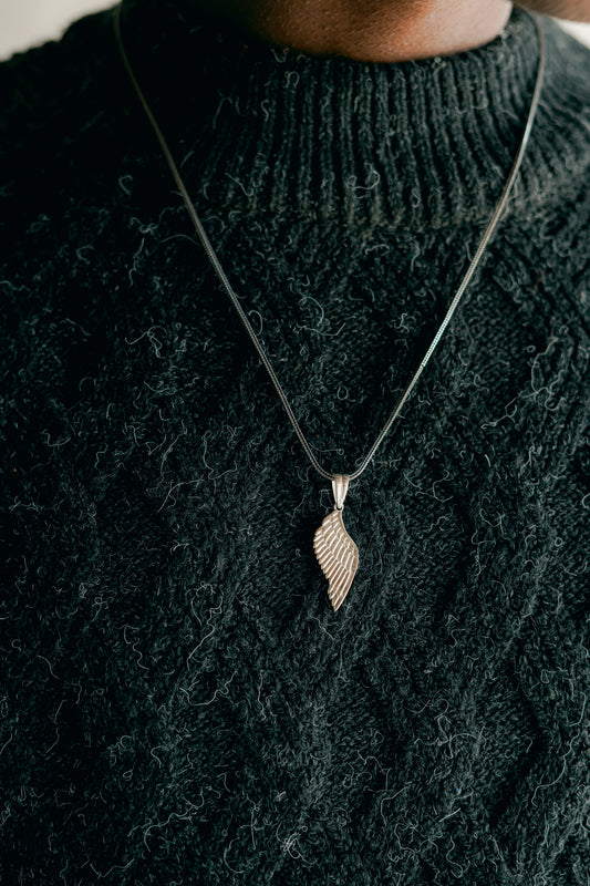 Ciondolo a forma di Ala o Piuma in Argento 925 indossato su una catenina sottile. Primo piano sul gioiello e sul collo del modello che indossa un maglione a trecce scuro.