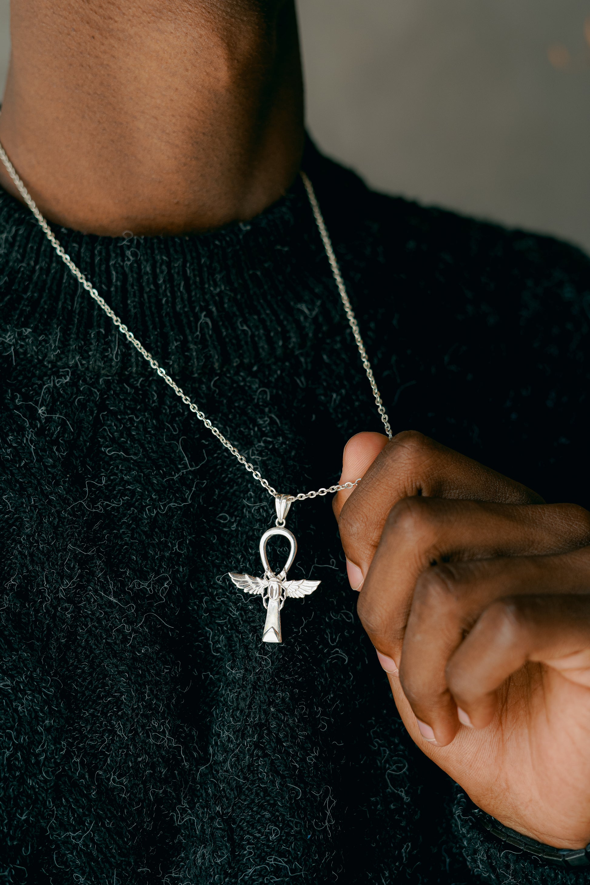 Ciondolo in Argento 925 a forma di Ankh alato, indossato su una catenina. Primo piano sul gioiello e sul collo del modello che indossa un maglione scuro.