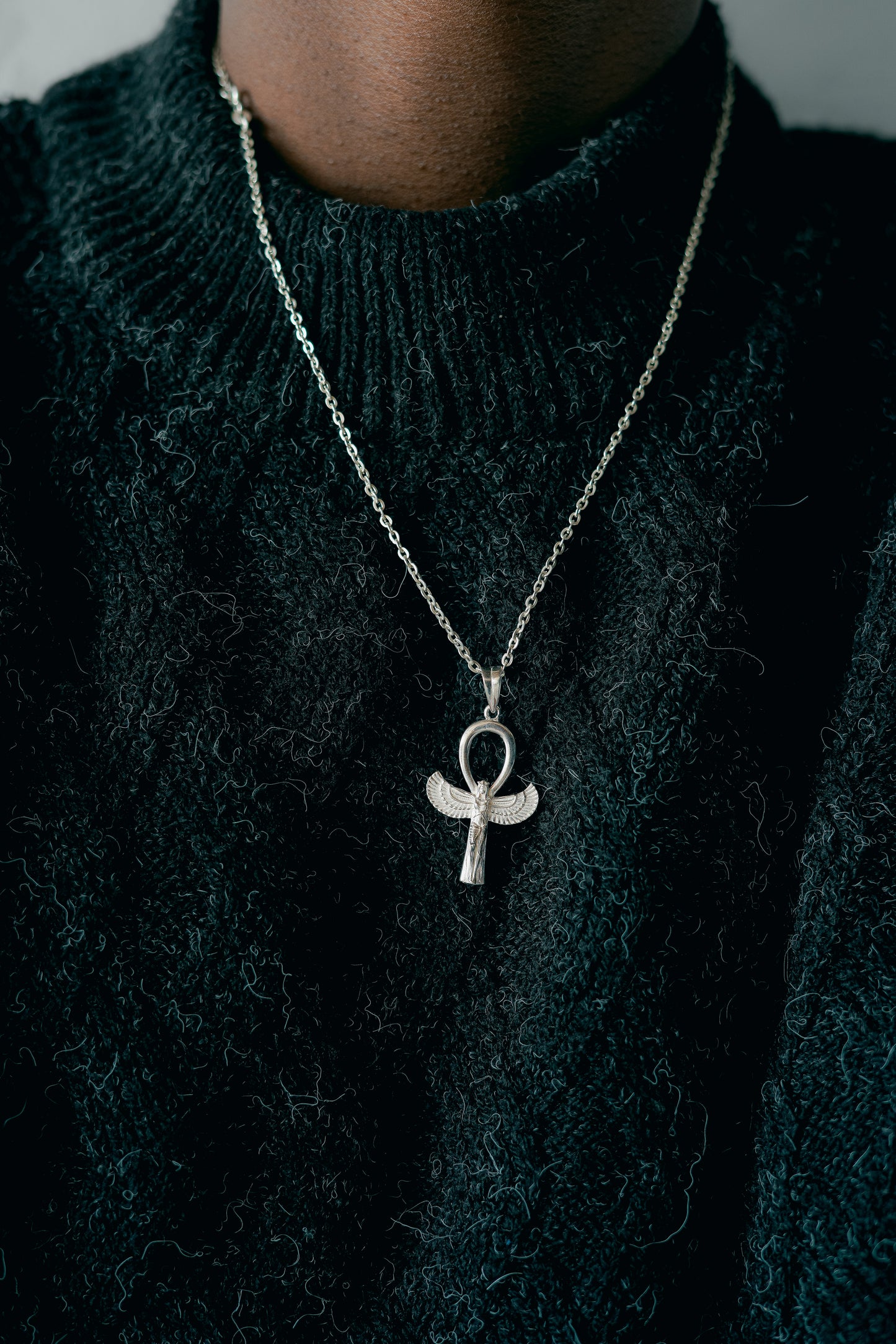Sterling 925 Silver Winged Ankh pendant (Guardian/Key of Life) on a chain. Close-up of the detailed jewelry against a dark knit sweater.
