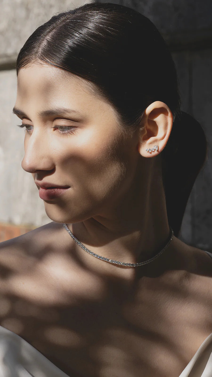 Dettaglio di una donna che indossa un set di tre collane tennis in argento 925 con pietre da 3mm. Il gioiello risplende alla luce del sole.